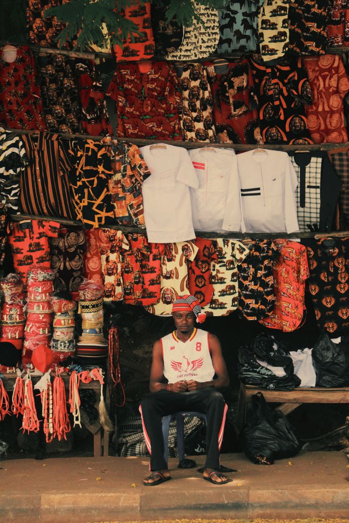 Colorful market stall in Enugu, Nigeria, featuring vibrant textiles and a vendor. A lively depiction of local commerce.