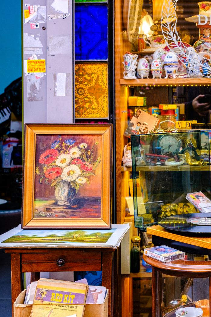 Colorful flea market booth featuring a framed floral painting and vintage collectibles.
