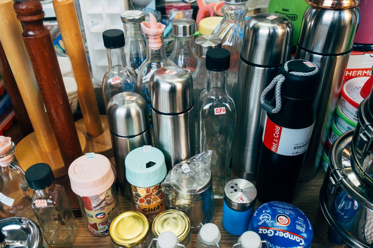 A variety of kitchen containers including bottles, jars, and thermos flasks on display.